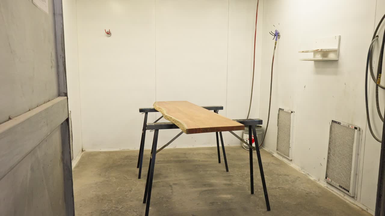 Slow motion push in on raw wood slab on riser inside paint spray booth
