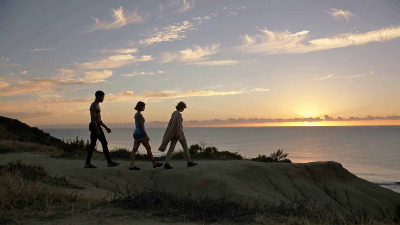 Walking prompted by sunset, three adults moving along sea cliff path, wearing long coat, footwear