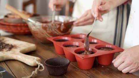 couple placing the chocolate cupcake batter into the baking pan, close up of two people preparing muffins