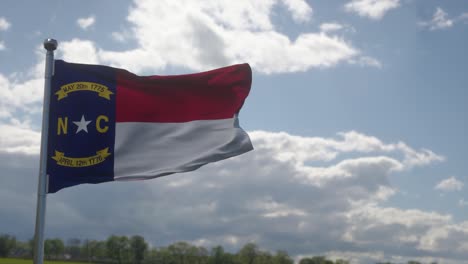 north carolina flag on a flagpole waving in the wind, blue sky background