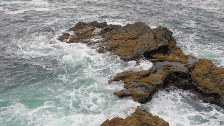 Campo lungo al rallentatore di onde oceaniche che si infrangono su una riva rocciosa.