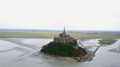 Volando-Detrás-Del-Mont-Saint-Michel-En-Francia,-Cuando-La-Marea-Del-Agua-Está-Baja.