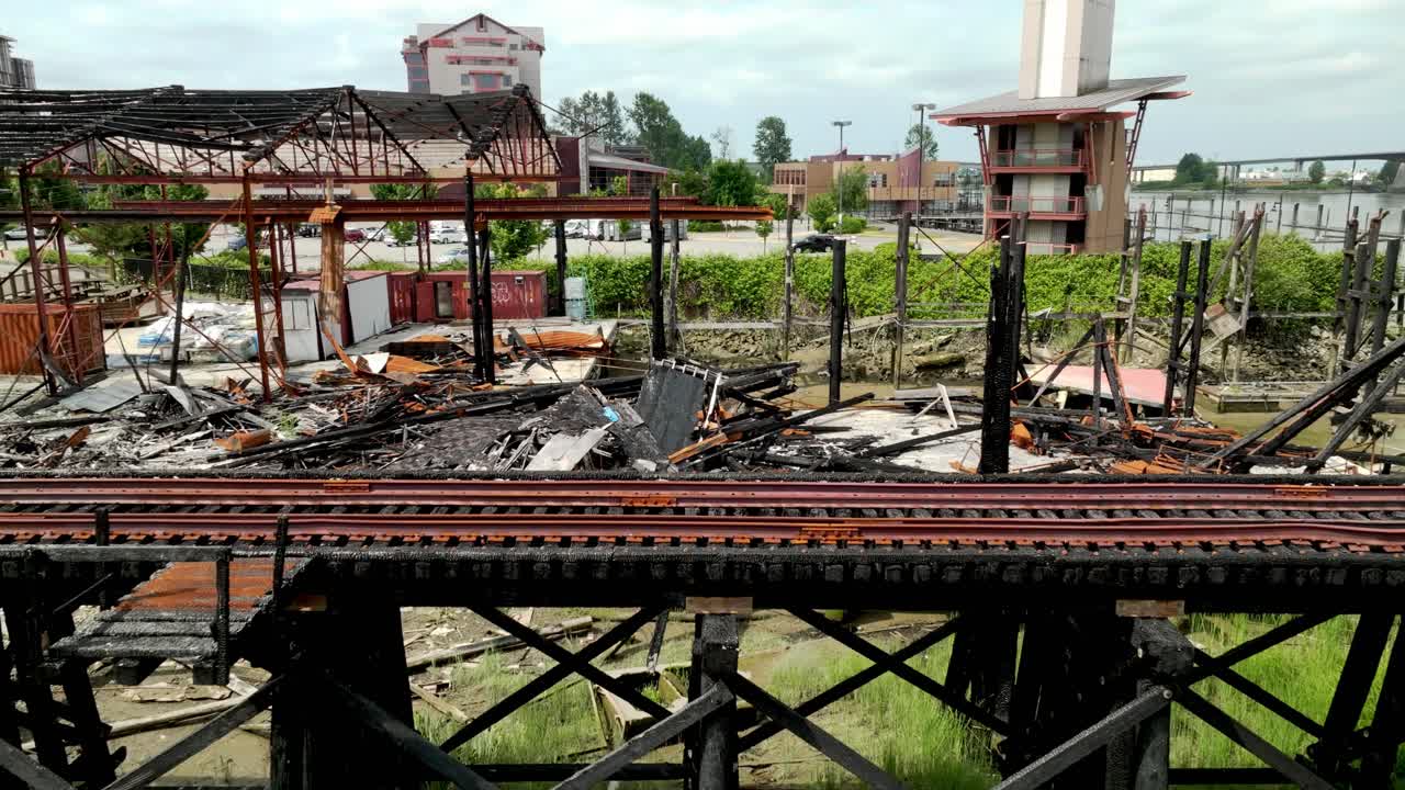 A Burnt Building Lies in Ruins Beside the Rail Bridge Along River Drive in Richmond, British Columbia, Canada - Aerial Pullback Shot