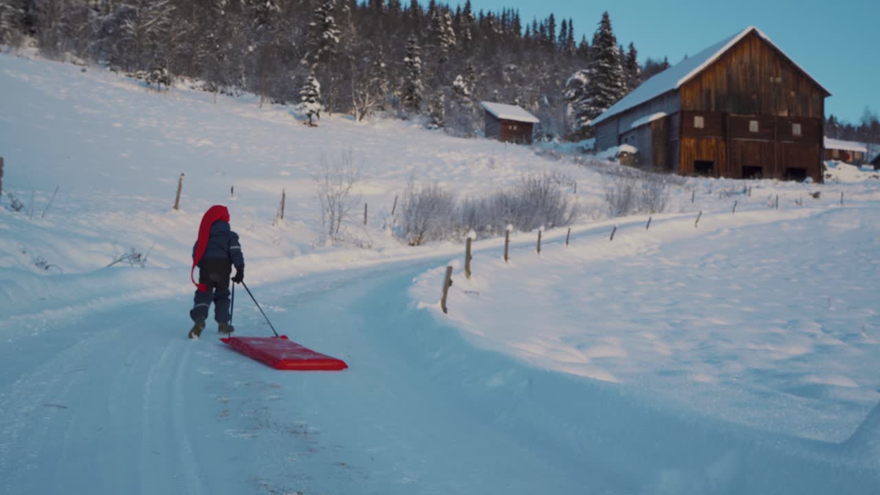 foto de un niño pequeño corriendo por la ladera mientras se divierte en la nieve, disfrutando del trineo usando un trineo de pala de plástico rojo en beitostolen, pueblo en el condado de innlandet, valdres, beito, noruega