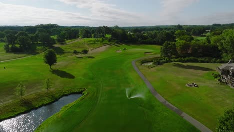 Toma-Aérea-De-Un-Hoyo-De-Golf-Con-Bunkers-De-Calle-En-Un-Club-De-Campo-Con-Rociadores-En-Funcionamiento