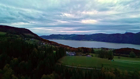 serene lake surrounded by hills and a forested landscape at dusk, clouds overhead, aerial view