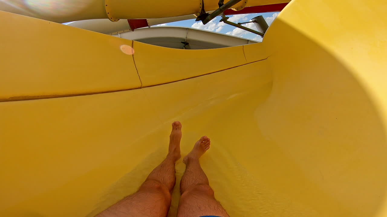 Fun down the water slide in summer day. Man goes down from water slide to swimming pool in aqua park. Quick way inside the pipe.