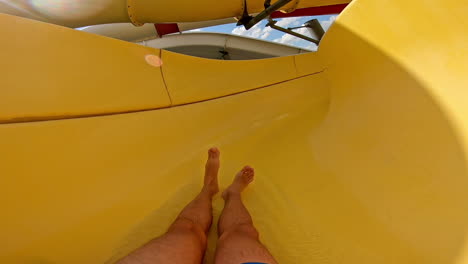 fun down the water slide in summer day. man goes down from water slide to swimming pool in aqua park. quick way inside the pipe.