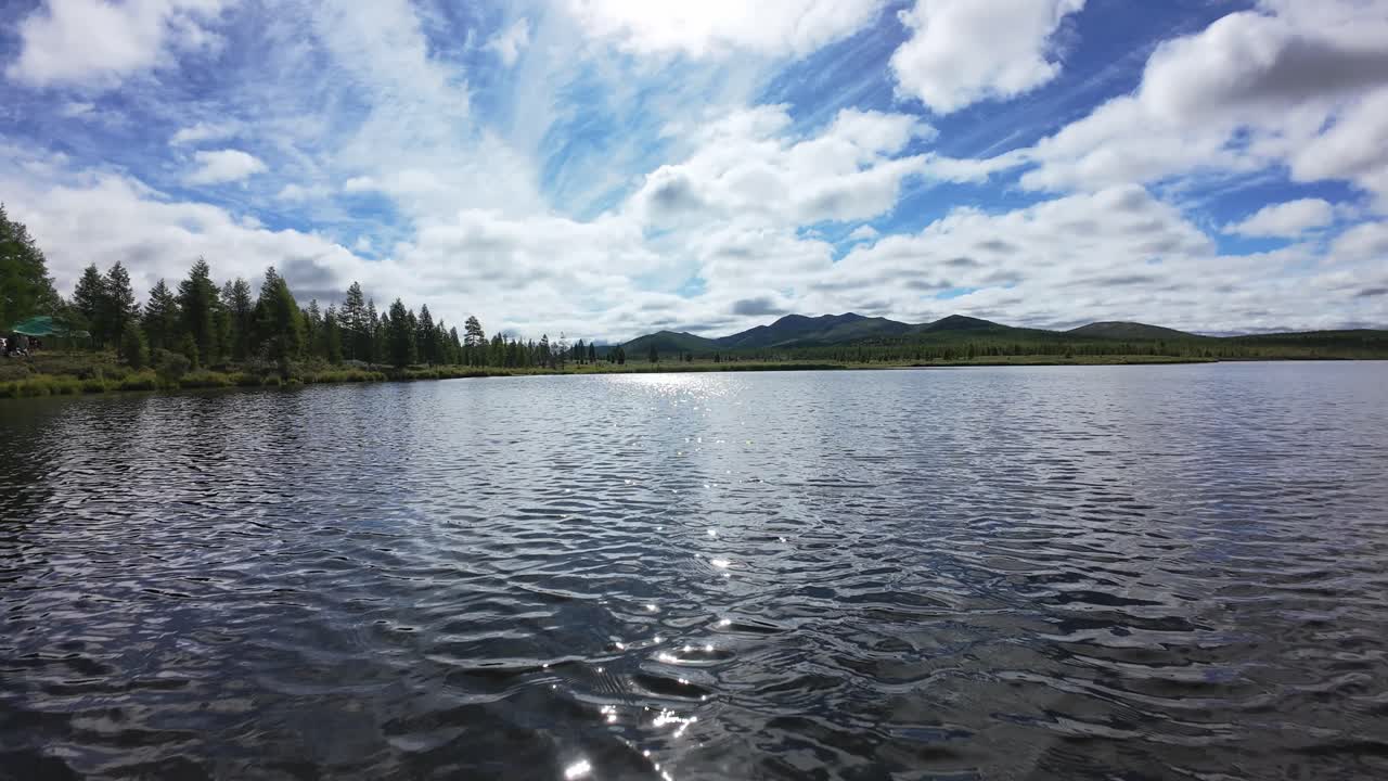 A drone captures breathtaking views of a tranquil lake with mountains and vibrant clouds overhead