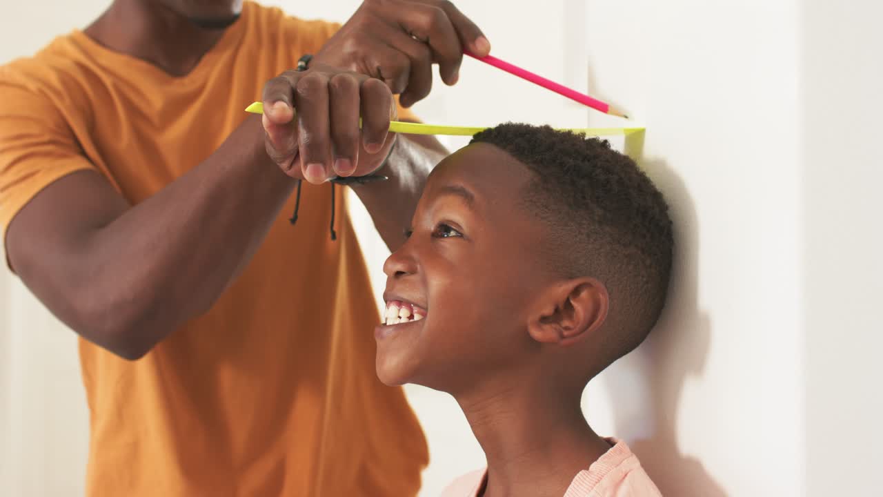 Father holding yellow tape, pink pencil, marking boy against white wall for height log, copy space