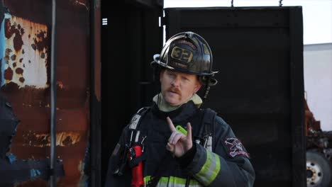 bombero en cámara lenta con bigote de manillar listo para la acción dando señal de balancín hacia la cámara panorámica del mediodía en el sujeto con equipo completo de bombero, incluida la chaqueta del casco