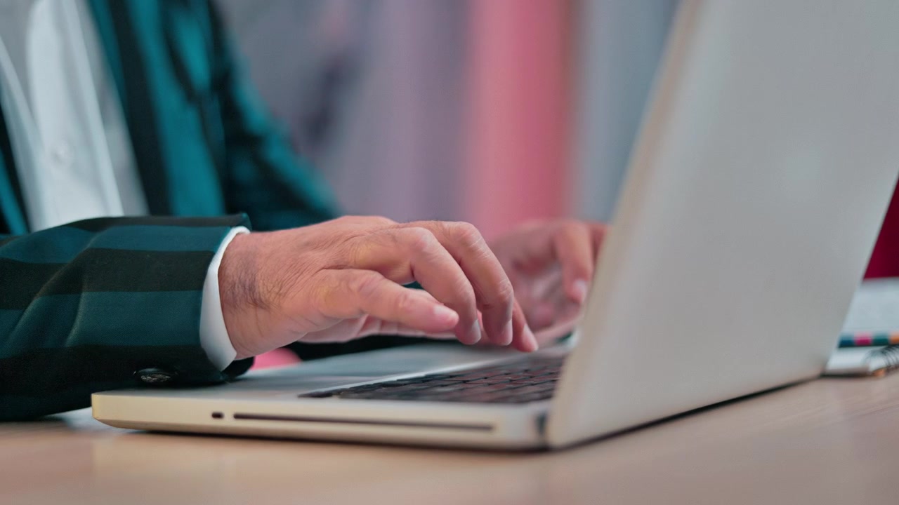 Close up shot of a mature male Fashion professional's hands operating a laptop for clothing design and creative project work.