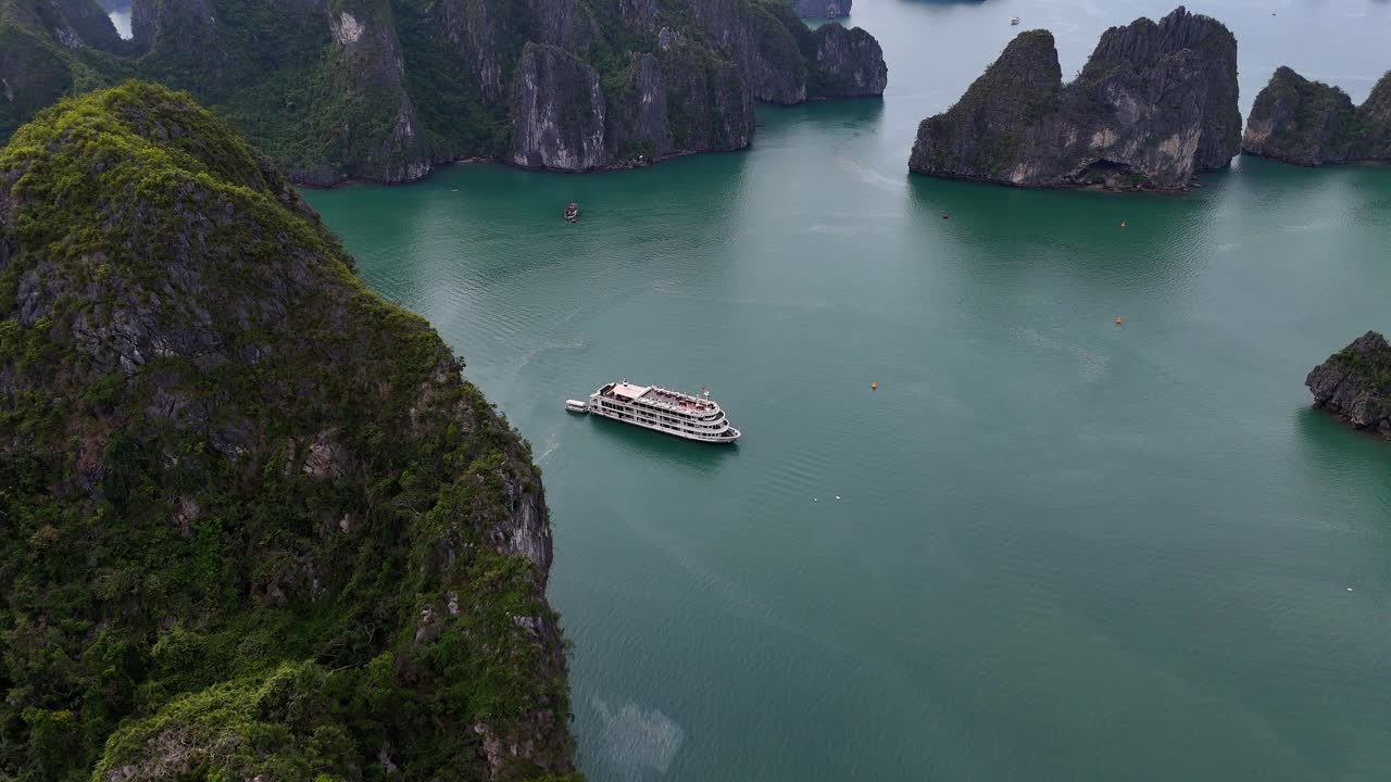 Reveal of a cruise ship in Halong Bay, Vietnam behind a large limestone rock