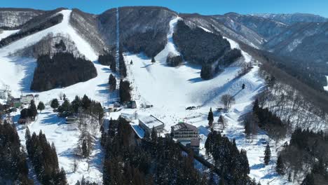 Wide-angle-orbiting-drone-shot-of-bottom-of-ski-run,-skiers-arriving-at-base-of-mountain-lining-up-for-the-chairlifts