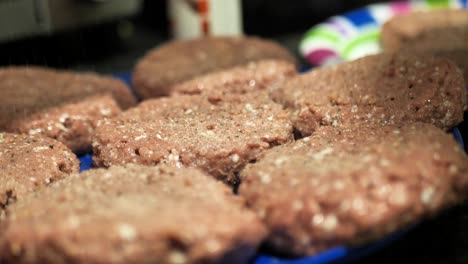 Seasoning-plant-based-burger-patties-on-a-blue-plate-for-a-summertime-barbecue-cookout,-close-up-shot-in-slow-motion-4k