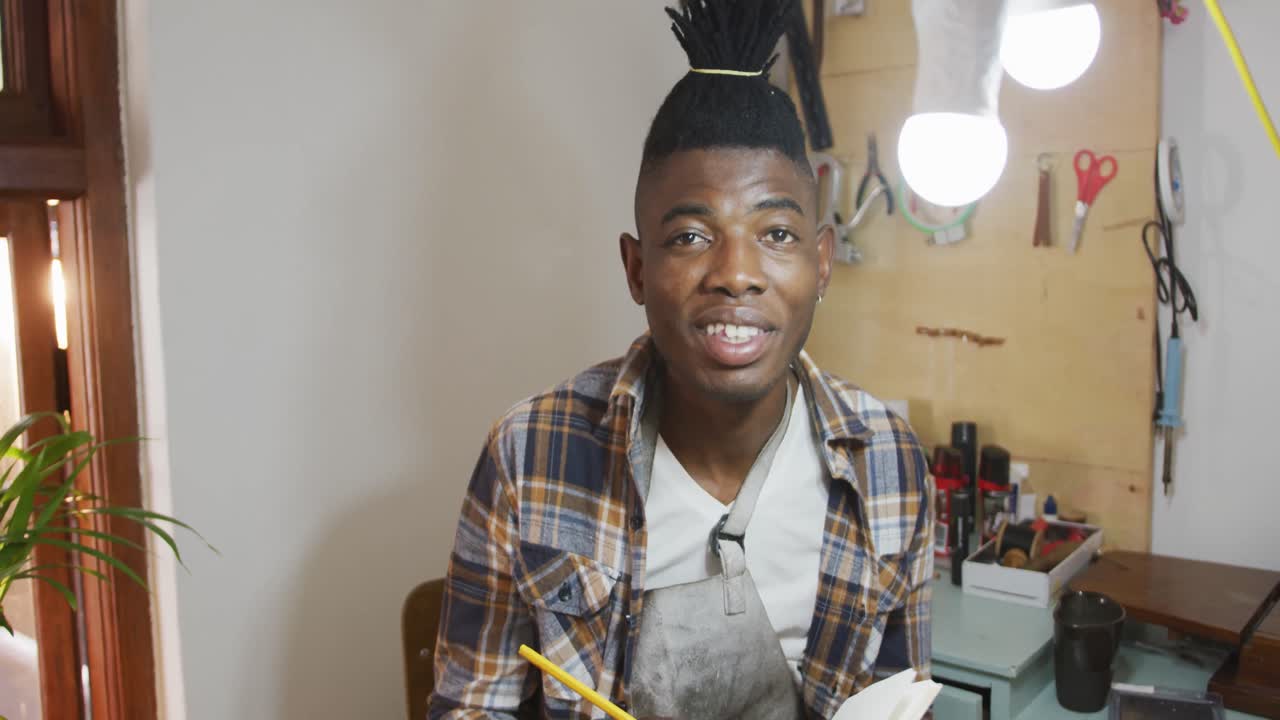 Ritratto di un felice artigiano afroamericano con il grembiule che sorride alla macchina fotografica in un laboratorio di pelletteria