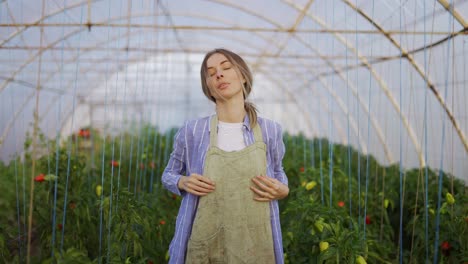 Young-woman-gardener-putting-on-apron,-ready-for-work-at-plant-shop-greenhouse