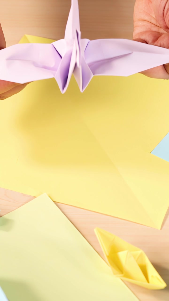 Person folder lilla origamitrane med gule papirbåde, set ovenfra, i klar, jævn belysning