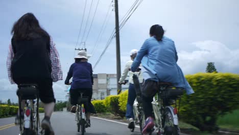 Group-of-female-bikers-riding-on-countryside-road-next-to-power-lines,-filmed-from-backside-following-riders