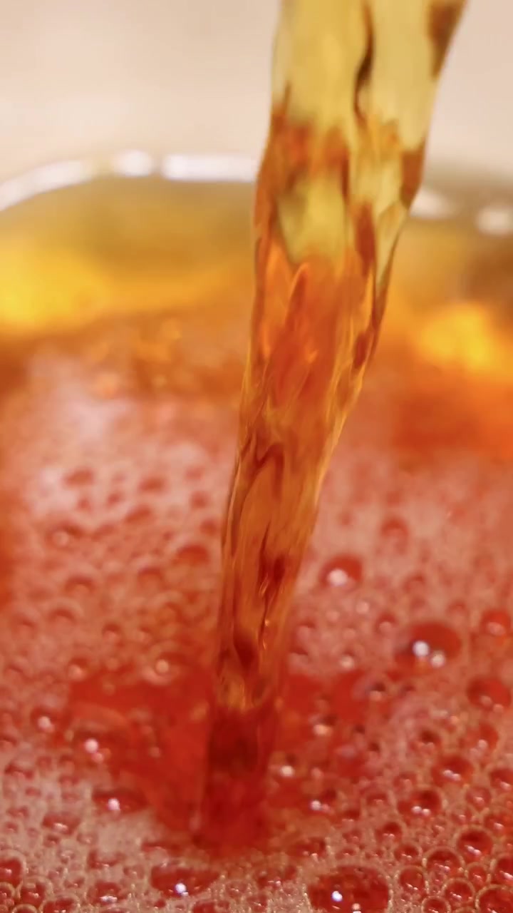 Primo piano di tè versato in una tazza, che crea bolle e schiuma con un'illuminazione calda.