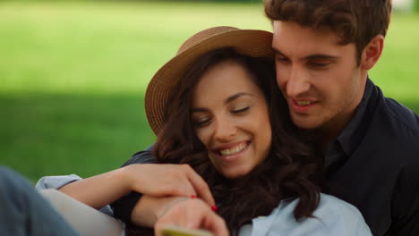 pareja linda buscando teléfono celular en un picnic. chica y chico usando un teléfono inteligente en el parque