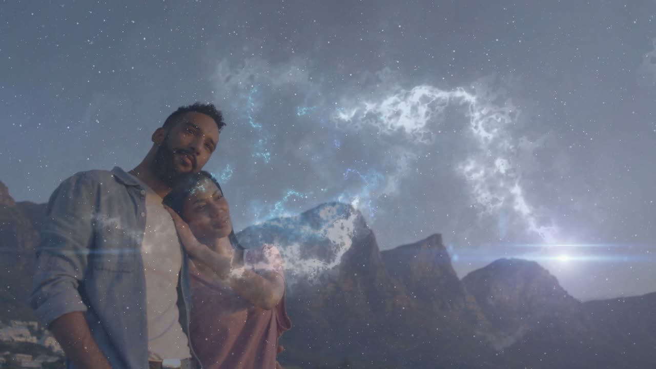 Hombre y mujer abrazándose al anochecer en la montaña, con una nebulosa inicial arqueándose por el cielo enmarcando su amor por viajar