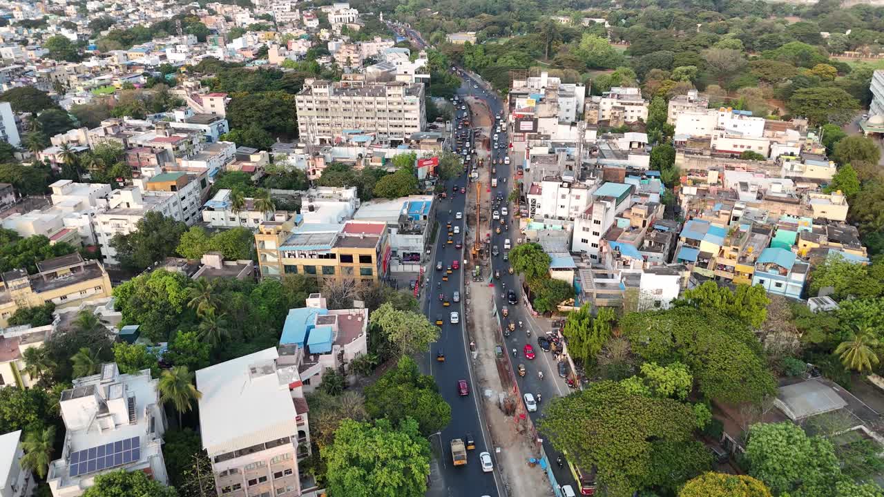 Anna Salai di Chennai è vista dall'alto, una strada trafficata con lavori in corso. Circondata da un mix di edifici residenziali e commerciali e spazi verdi, l'immagine cattura una vivace scena urbana.