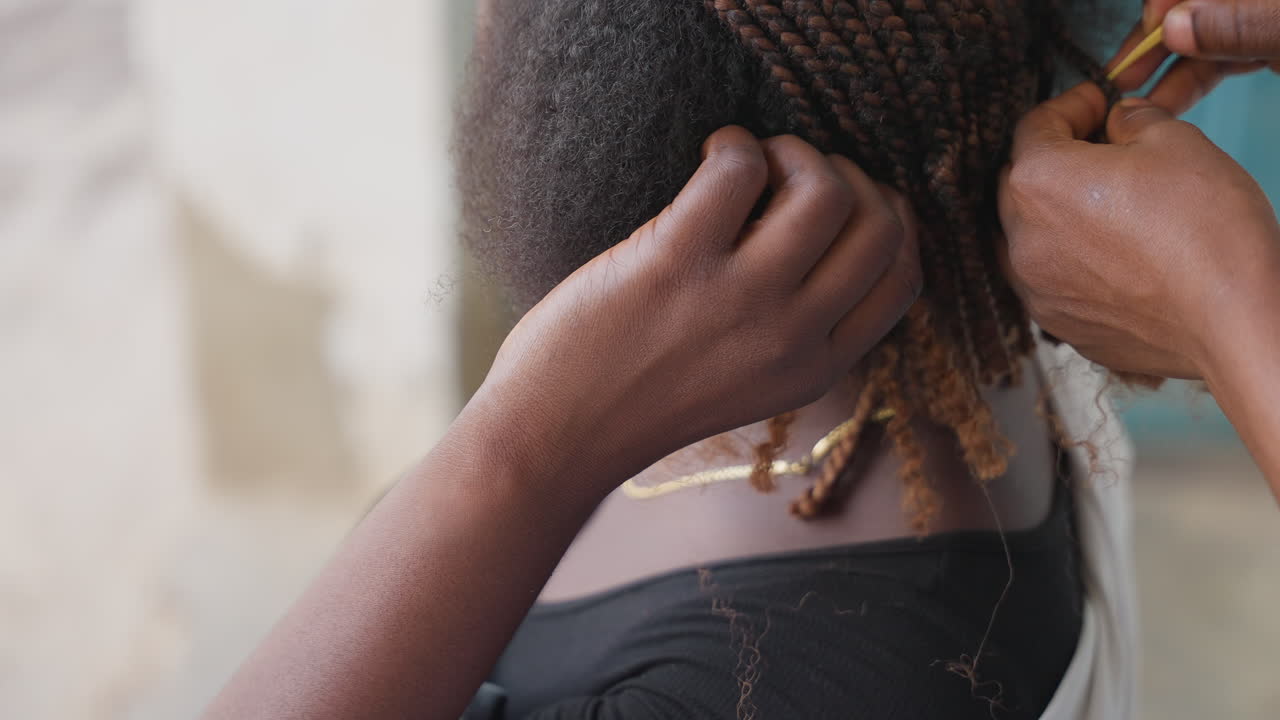 Primo piano di intreccio di capelli. Focus su dita e radici durante il processo professionale di trecciatura dei capelli. Lavoro preciso delle dita in luce naturale che cattura l'intricata maestria dell'intreccio dei capelli.