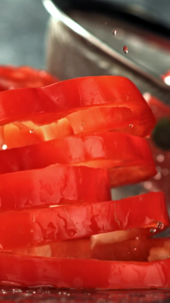 Fette fresche di peperone rosso che cadono nell'acqua al rallentatore