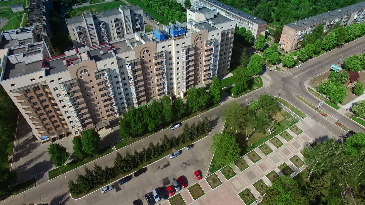 Flying over the multi-storied buildings with nice well-kept territories around and lots of trees and greenery. View of the city from air.