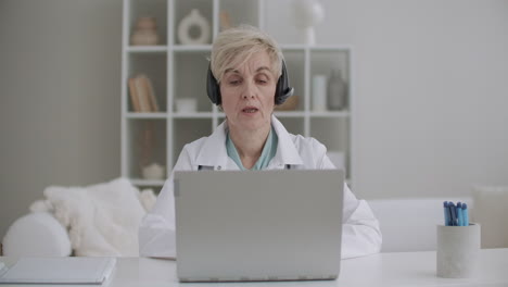 female aged gynecologist is consulting online talking with patient by videochat on laptop working remotely by internet