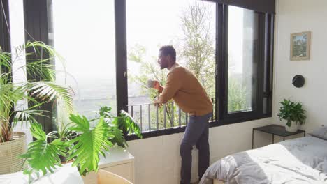happy african american man looking through window and drinking coffee