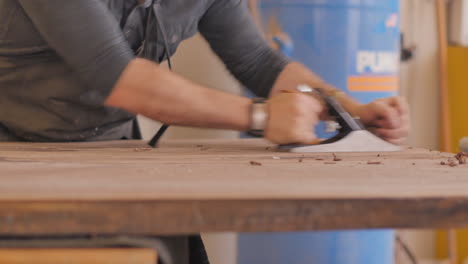 a craftsman woodworker is using a planer to make a custom wood table top smooth and even