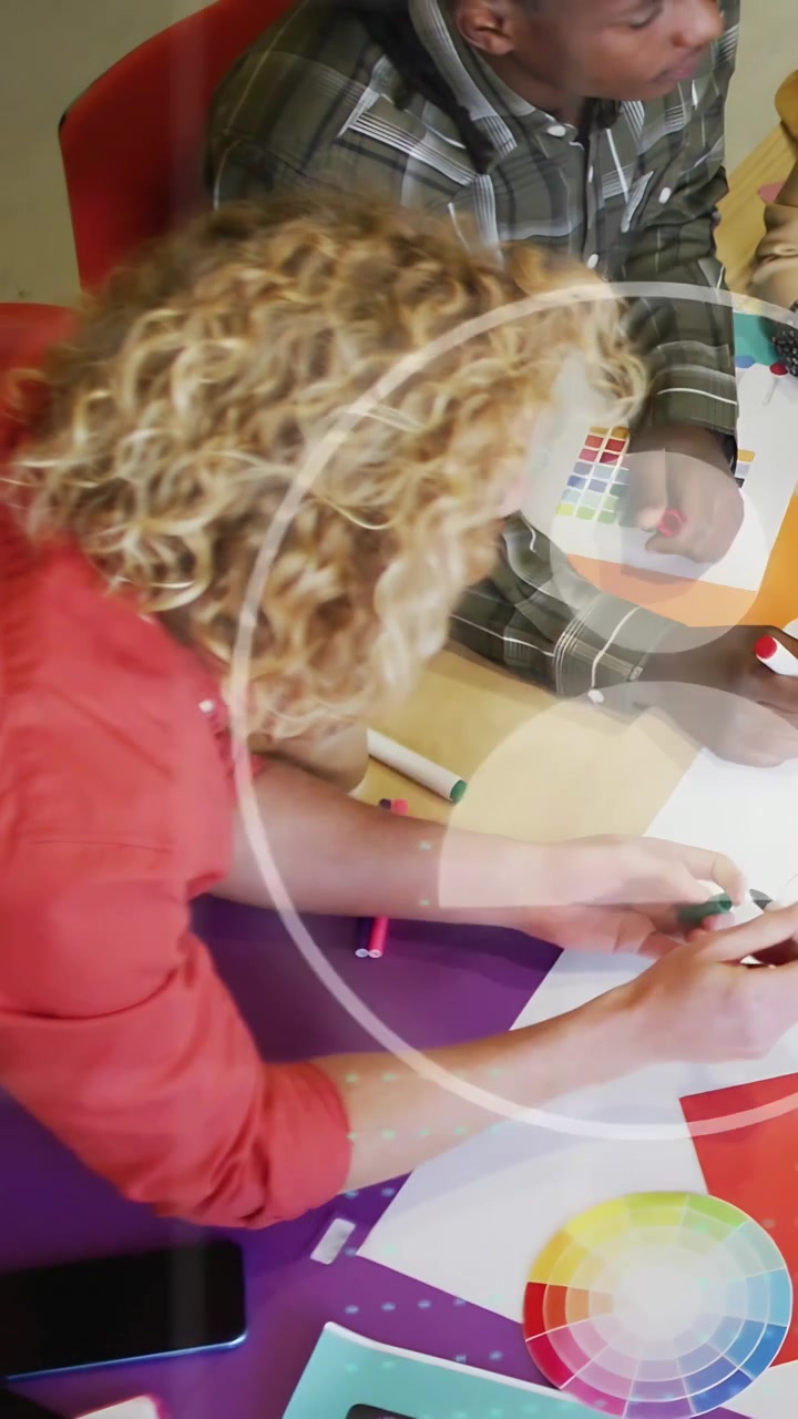 Verticale video: Ontwerpers testen kleuren, vrouw pakt pen, man gebruikt stalenoverlay die tafel bedekt.