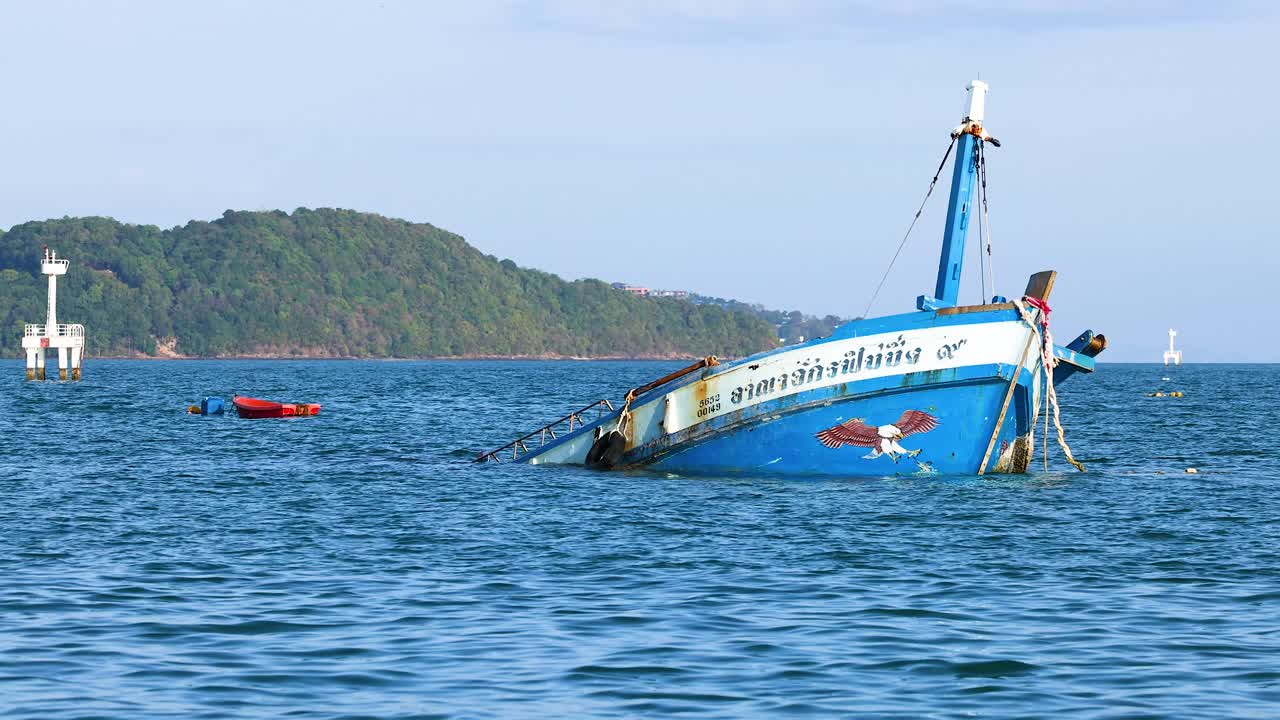 A fishing boat gradually sinks in the ocean near Phuket, Thailand, under clear skies with surrounding islands visible