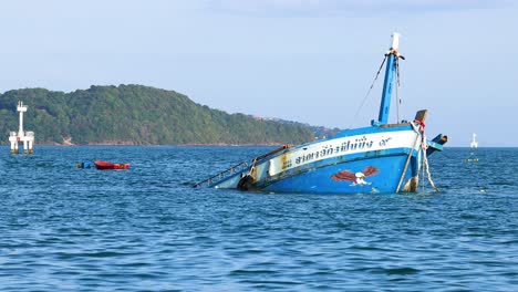 a fishing boat gradually sinks in the ocean near phuket, thailand, under clear skies with surrounding islands visible