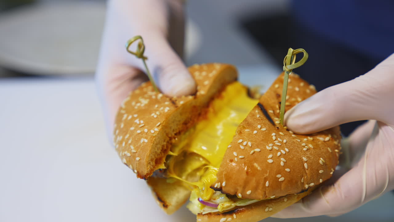 Cutted in a half tasty appetizing cheesburger. Chef in gloves shows a hamburger with meat cutlet and cheese.