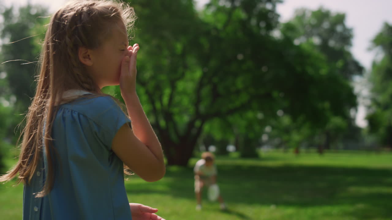 chica graciosa rascándose la nariz en sunny park. niño lindo limpiándose la cara desde atrás.