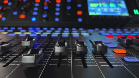 Moving-faders-on-digital-mixing-console,-closeup-view,-blurry-lights-in-background