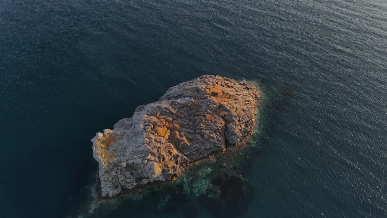 En cirkulær droneoptagelse af en stenet ø under solnedgangen