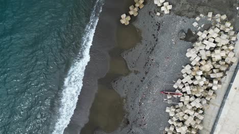 top down aerial view of philippine village island coastline with turquoise ocean waters, grey sand, and concrete tetrapods