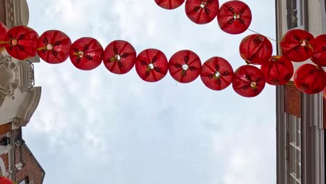 a view of red lanterns strung across the sky between two buildings, set against a cloudy backdrop.