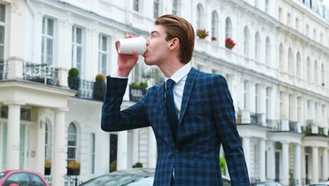 stylish young man carrying coffee standing on city street