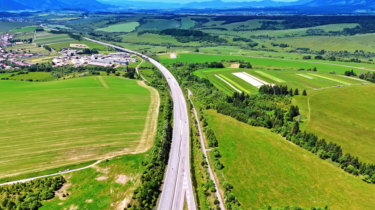 Winding road through green fields. A highway curves through lush green fields and farmland under a clear blue sky, showcasing natural beauty