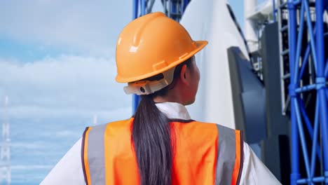 close up back view of a female engineer wearing safety helmet looking around while standing with arms akimbo with space shuttle