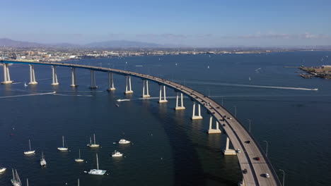 Drone-Volando-Sobre-Los-Vehículos-Que-Conducen-En-El-Puente-Coronado-Sobre-La-Bahía-De-San-Diego-Con-Chula-Vista-Y-Ciudad-Nacional-En-Segundo-Plano-En-San-Diego-California,-Estados-Unidos