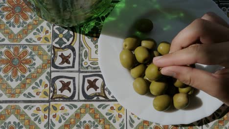 Hand-taking-olive-from-plate-on-mosaic-table-in-terrace,-top-view,-Mediterranean