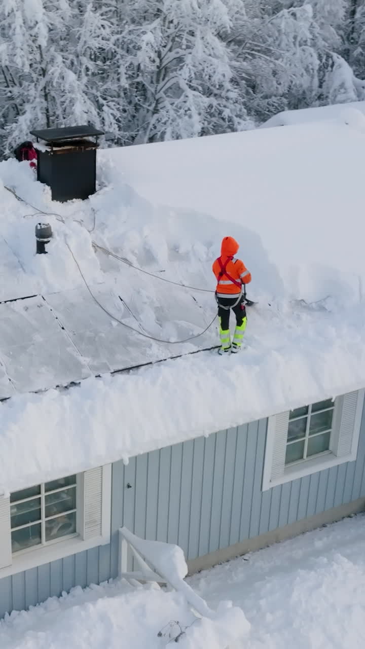 Aerial view around a worker shoveling snow a house roof with solar panels