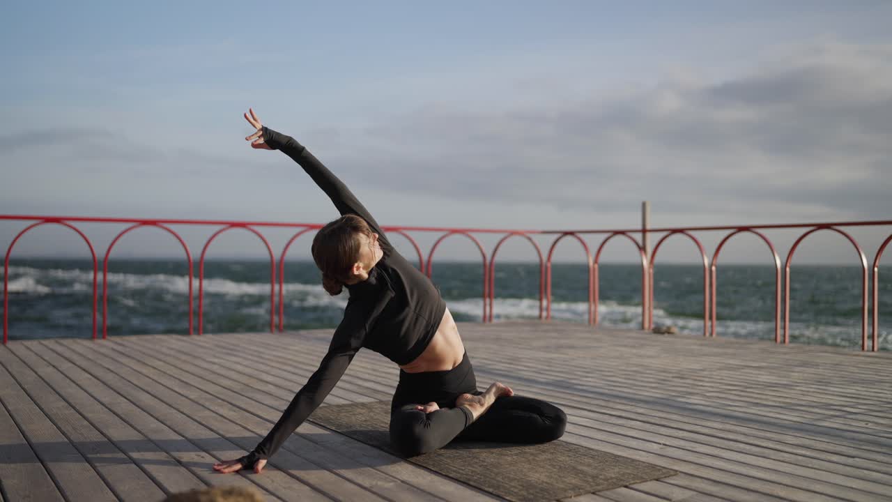 mujer practicando yoga en un muelle de madera con vistas al océano
