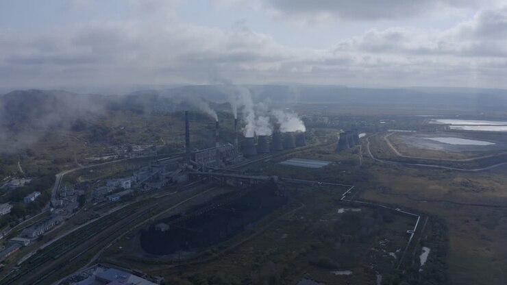 Slow push back shot of a coal-fired power station with its chimneys and funnels releasing white and grey smoke into the air on a sunny and cloudy day